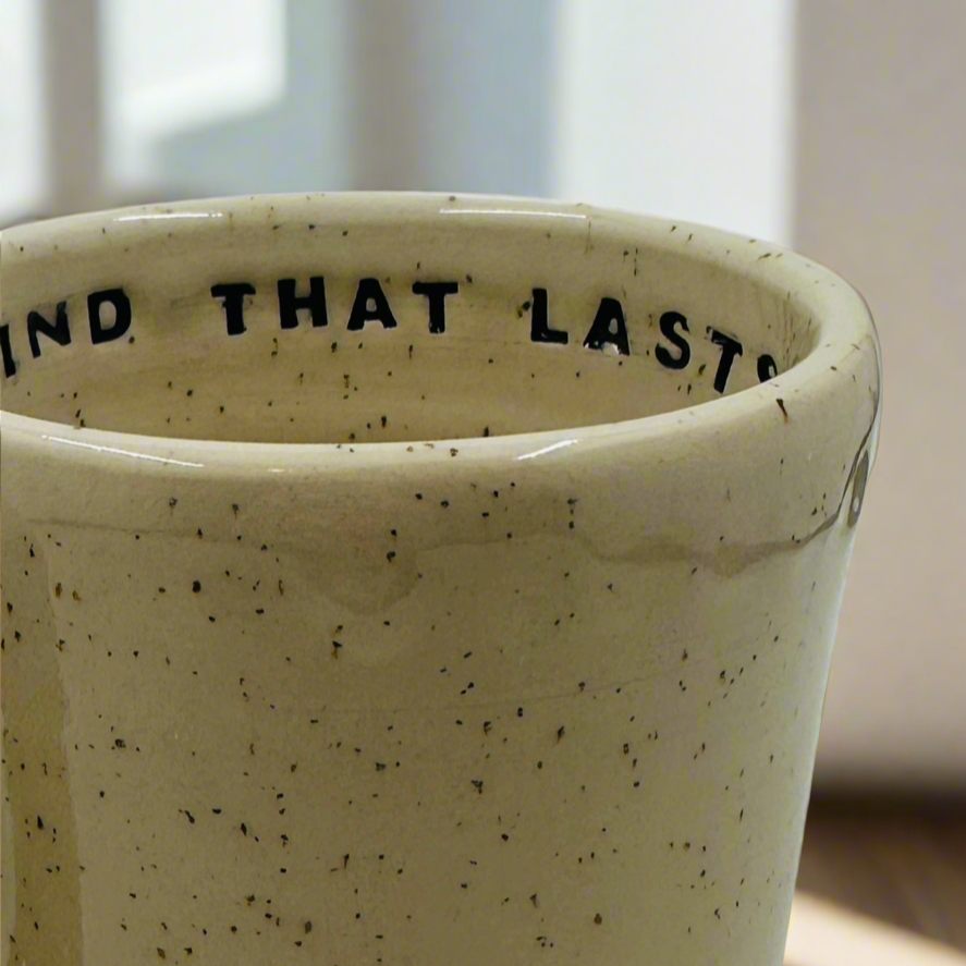 Speckled ceramic cup with text 'IND THAT LAST' on a blurred background