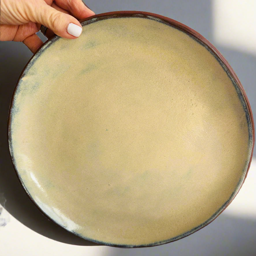 Hand holding a ceramic plate with a beige interior and black exterior rim on a light gray background