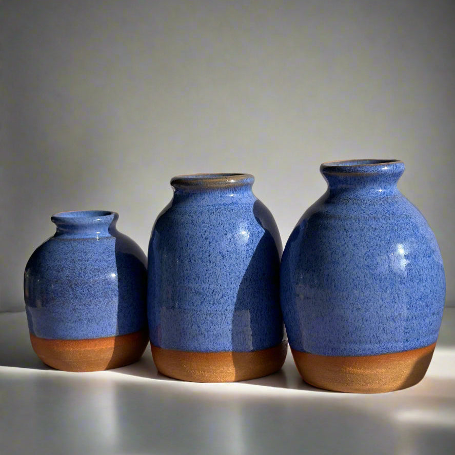Three blue ceramic vases with brown bases leaning against a gray wall.