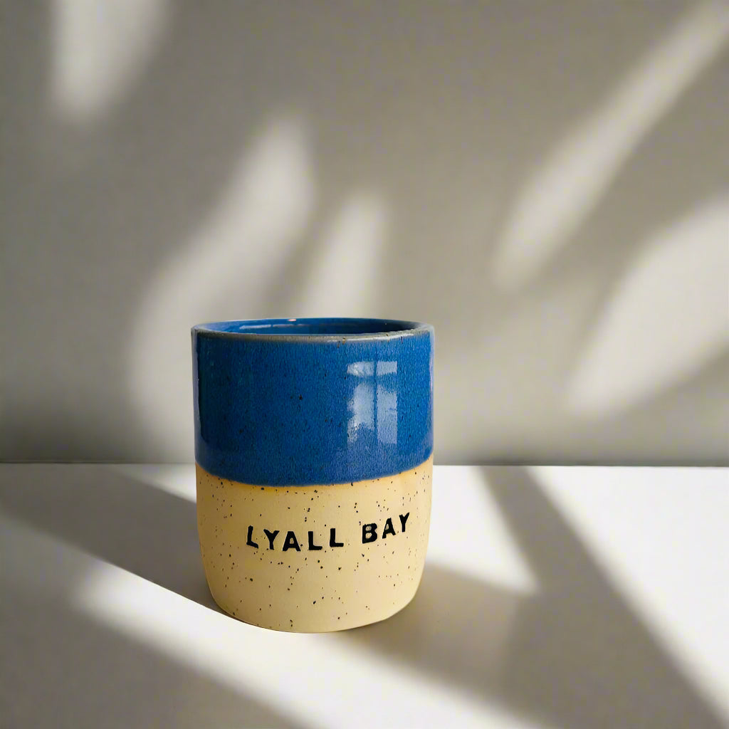 Ceramic cup with blue top and beige bottom, featuring 'LYALL BAY' text on a white background.