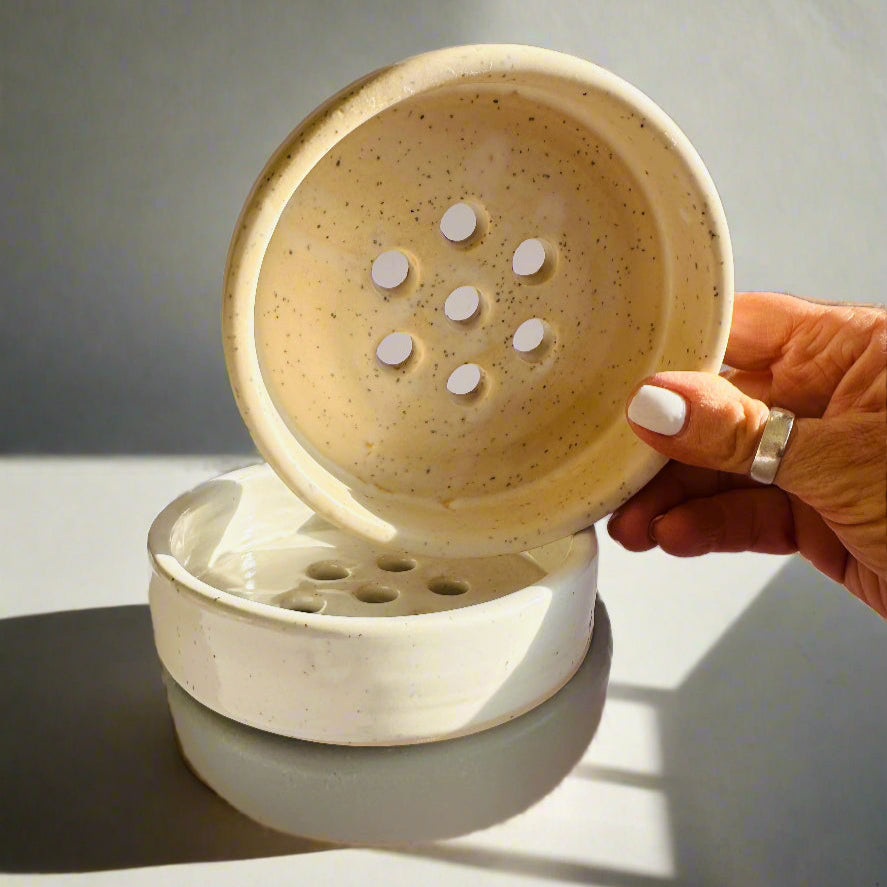 Hand holding a ceramic soap dish with soap tablets on a neutral background