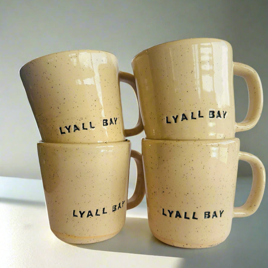 Four beige mugs with 'LYALL BAY' text on a light background