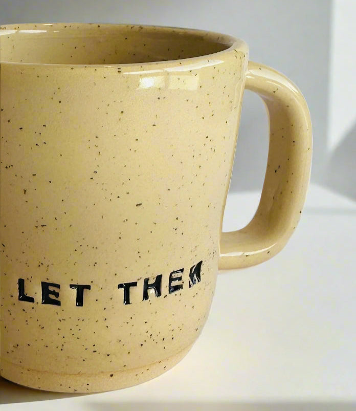 Beige speckled mug with 'LET THERE BE' text on a light gray background